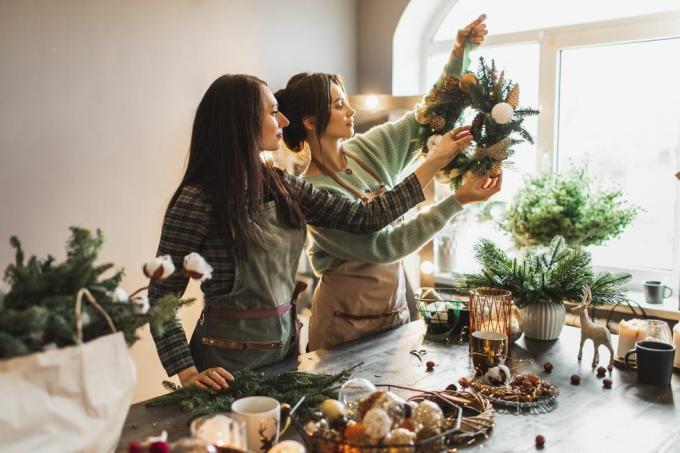 Taze çam dalları ve şenlikli süslemeler kullanarak Noel çelengi yapan iki kadın